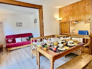 Ein gemütlicher Raum mit einem Holzespeisetisch, gedeckt für das Frühstück, einer roten Couch mit Kissen mit Herzmuster und einem Holzkabinett über dem Tisch.