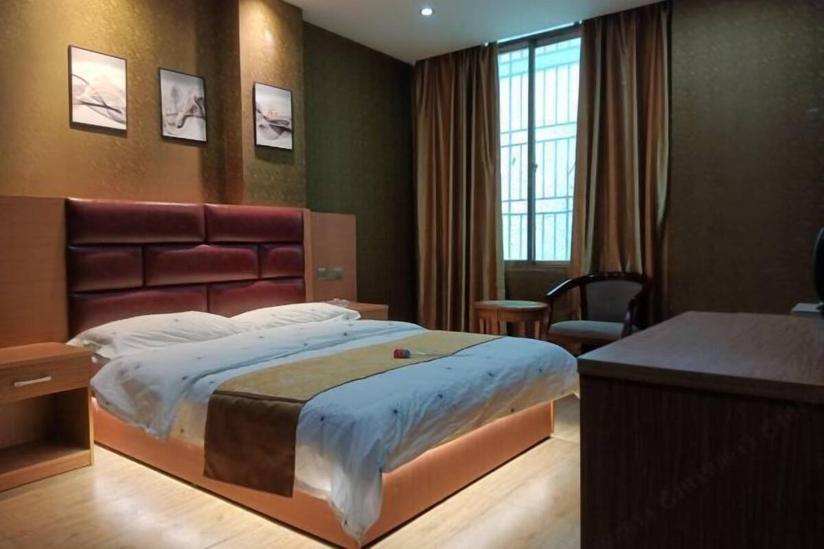 Une chambre d’hôtel avec un grand lit, un bureau, une chaise, une petite table et une fenêtre avec des rideaux.