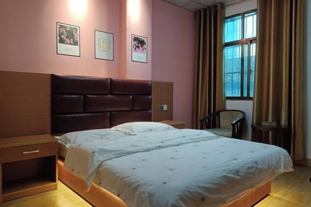 Une chambre à coucher avec une tête de lit en bois, un lit avec une literie blanche, une table de chevet, une chaise et une fenêtre avec des rideaux.
