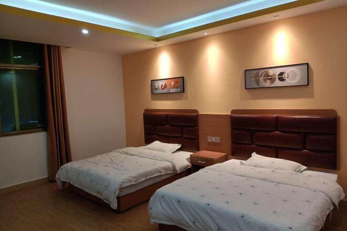 Une chambre d’hôtel avec deux lits, une fenêtre avec des rideaux et des œuvres d’art accrochées aux murs.