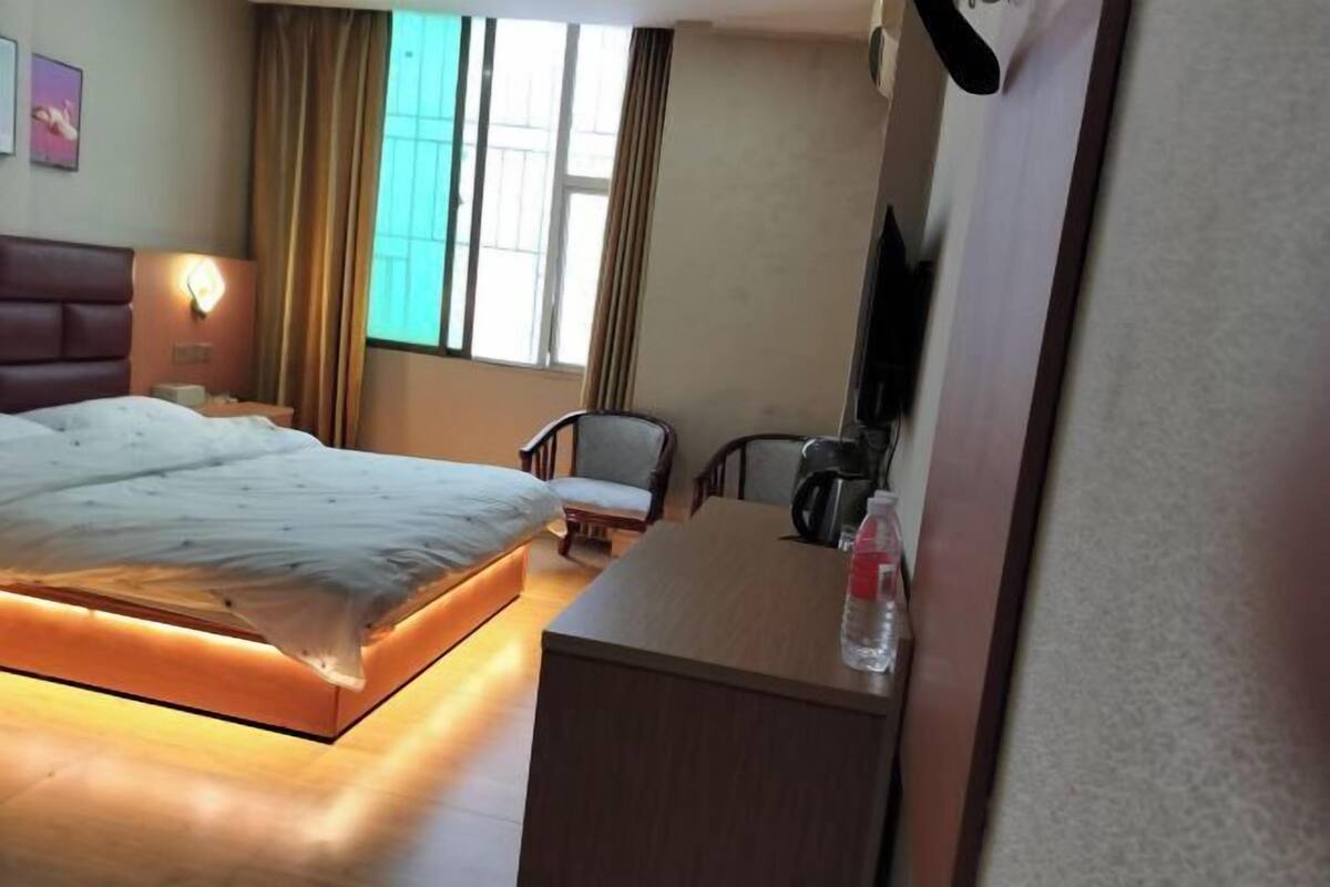 Une chambre d’hôtel avec un lit, un bureau, une chaise, une télévision et une fenêtre avec des rideaux.