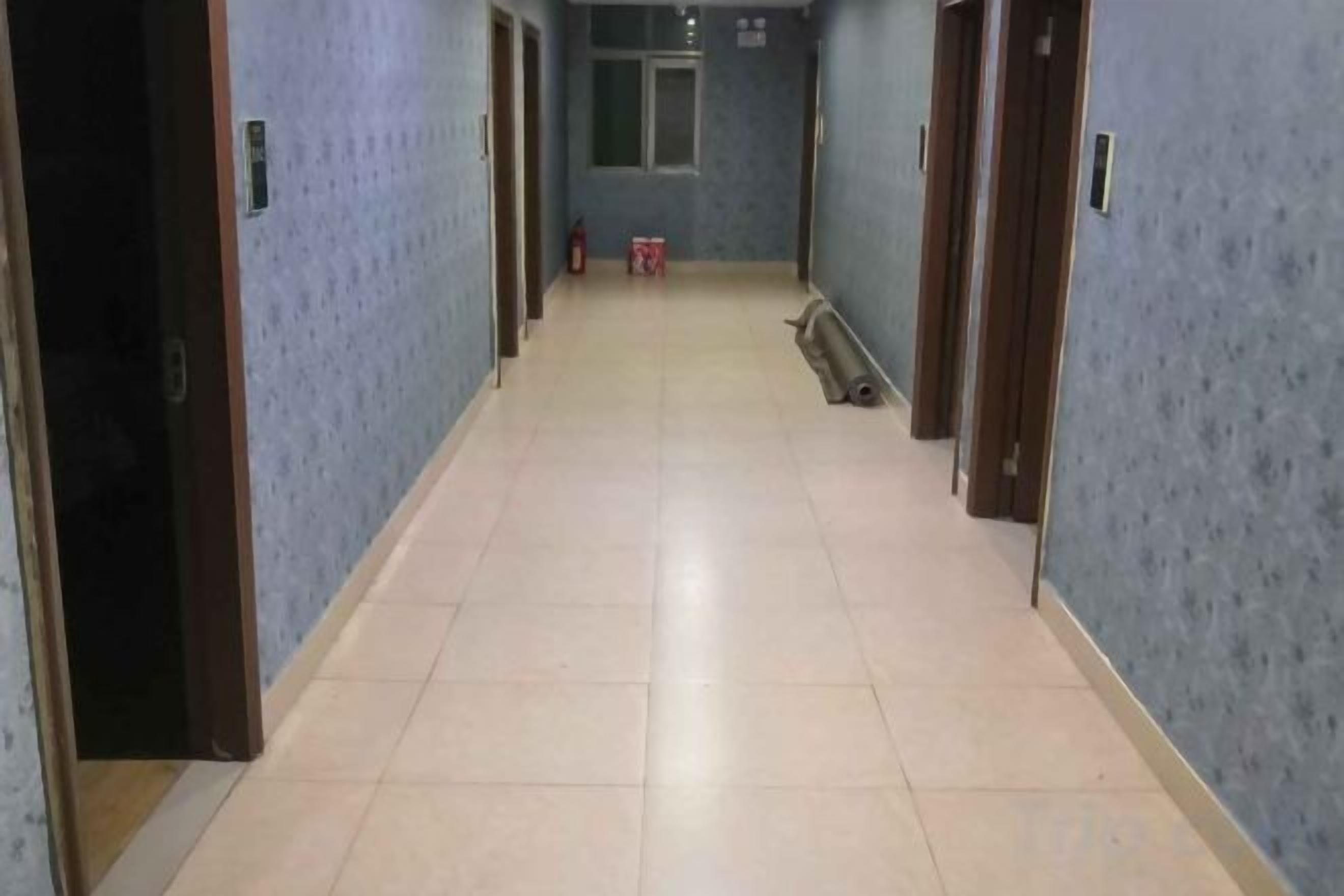 Un pasillo con puertas a ambos lados, suelo de baldosas y un extintor a lo lejos.
