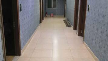 Un pasillo con puertas a ambos lados, suelo de baldosas y un extintor a lo lejos.
