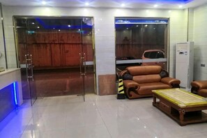 A reception area with a glass door, a brown leather sofa, a wooden coffee table, and a car visible through the glass. - Youshang Boutique Hostel (Dongguan)