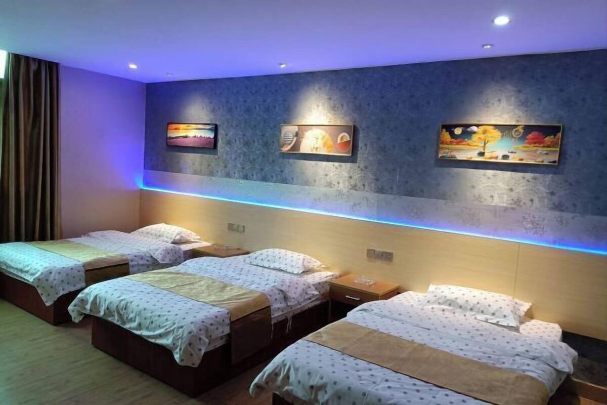 Une chambre d’hôtel avec trois lits, un téléviseur fixé au mur et un luminaire au plafond.