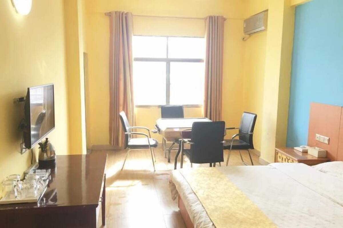 Une chambre d’hôtel avec un lit, un bureau avec deux chaises, une télévision et une fenêtre avec des rideaux.