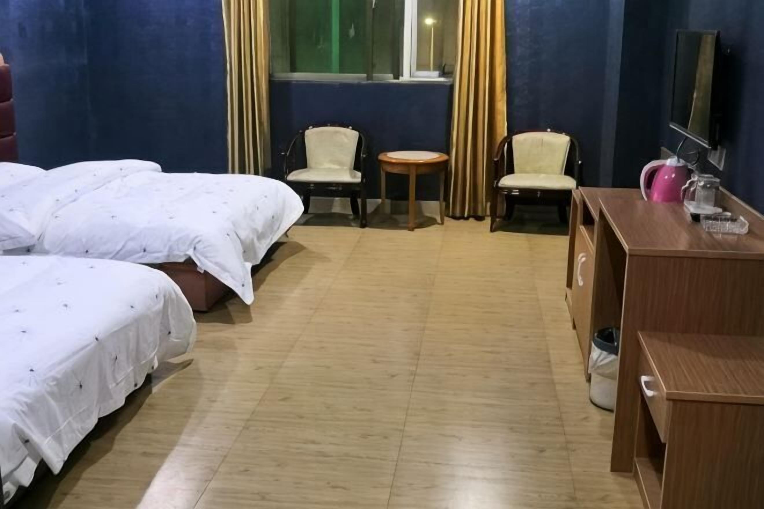 A hotel room with two beds, two chairs, a small table, a desk, and a television.