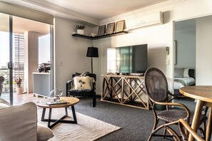 A modern living room with a flat-screen TV, a coffee table, a sofa, and a dining area with a wooden table and chairs.