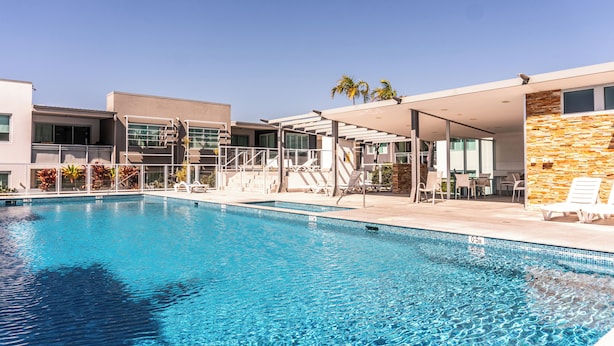 A modern hotel with a swimming pool, outdoor seating, and a stone wall.