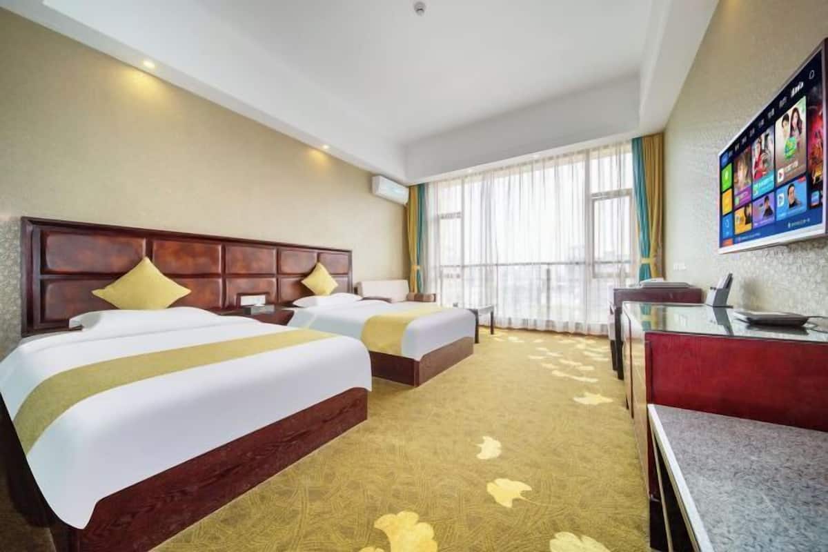 A hotel room with two beds, a desk, and a television mounted on the wall.