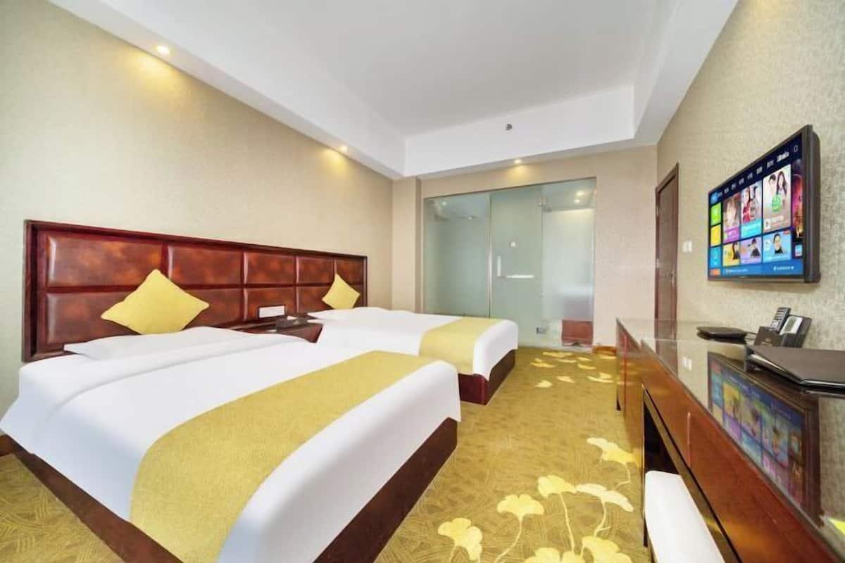 A hotel room with two beds, a desk, a TV, and a glass shower area.