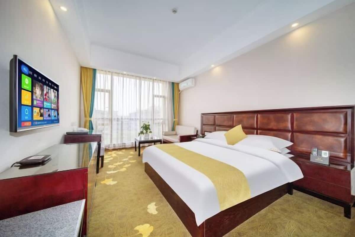 A hotel room with a large bed, a desk, a TV, and a window with curtains.