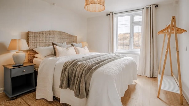 Un dormitorio con cama, mesita de noche, lámpara y ventana con cortinas.