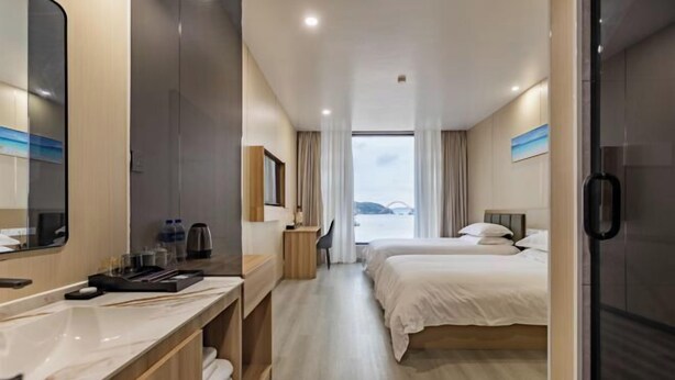 A hotel room with a large mirror, a desk with a chair, two beds, and a view of the outdoors. - TongQianWan Hotel (Xiangshan)