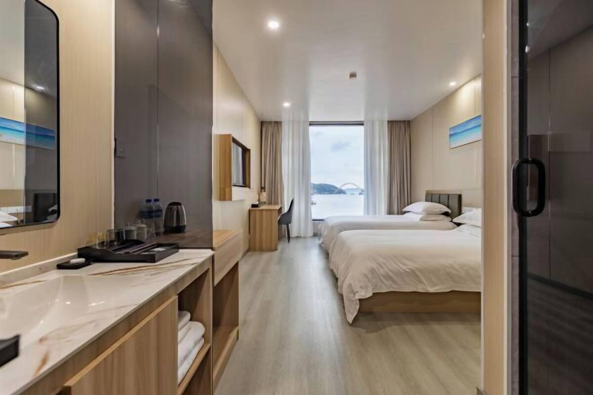 A hotel room with a large mirror, a desk with a chair, two beds, and a view of the outdoors.