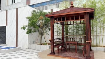A wooden gazebo with a bench, situated on a tiled patio with a checkered pattern.