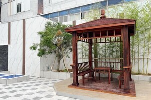 Un pabellón de madera con un banco, ubicado en un patio empedrado con un diseño de tablero de ajedrez.