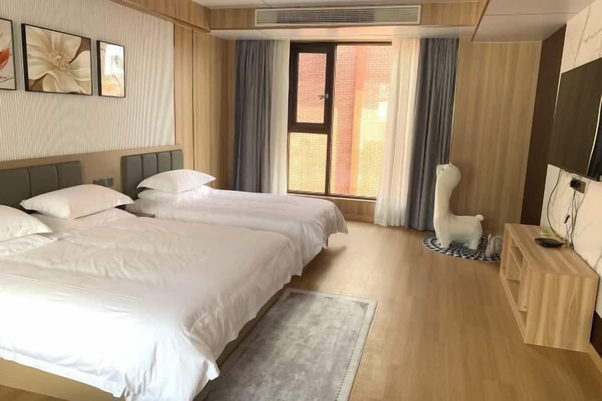 A hotel room with two beds, a TV, a desk, and a window with curtains.