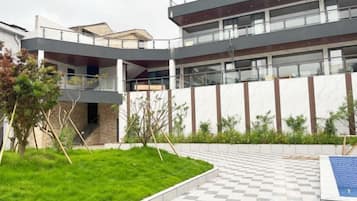 A modern building with a curved facade, a rooftop terrace, and a well-maintained garden area.