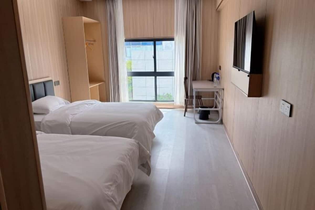 A hotel room with two beds, a TV, a desk, and a window with curtains.