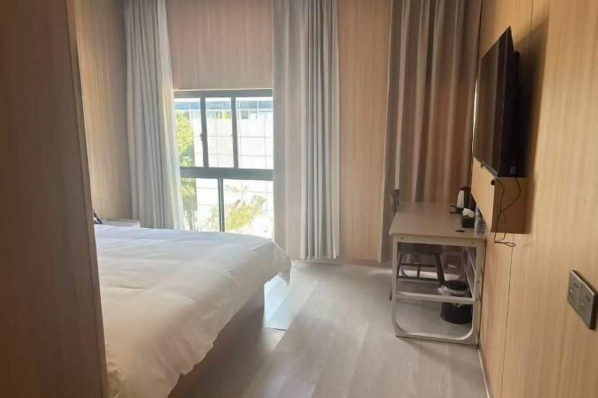 A hotel room with a bed, a desk, a TV, and a window with curtains.