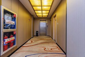 A hotel corridor with a patterned carpet, a vending machine, and an elevator in the distance. - TongQianWan Hotel (Xiangshan)
