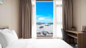 A hotel room with a bed, a desk, and a view of boats on the water.