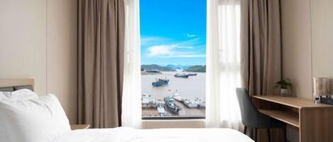 A hotel room with a bed, a desk, and a view of boats on the water.