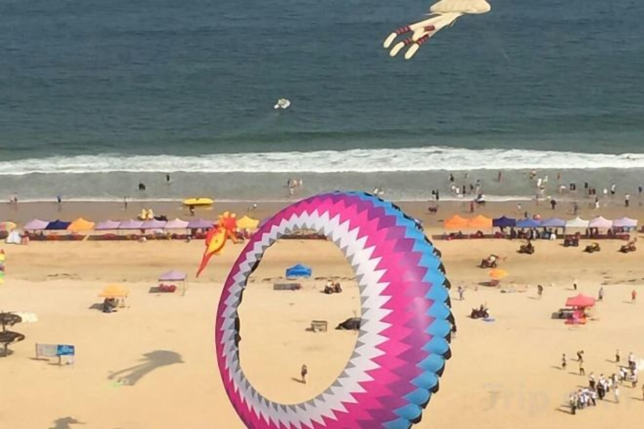 A beach with a large circular object, possibly a kite, in the foreground.