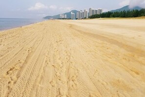 A wide sandy beach with footprints, a clear sky, and buildings in the background. - Haizhimeng Luxury Holiday Apartment Yangjiang Hailing Island Shili Yintan (Yangjiang)