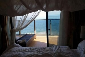 Une chambre à coucher avec un lit, une table de chevet et une vue sur l’océan grâce à de grandes fenêtres.