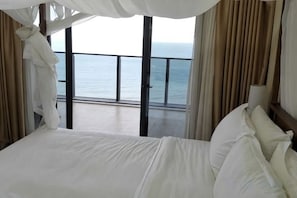 A hotel room with a large bed, a balcony with a view of the sea, and curtains. - Haizhimeng Luxury Holiday Apartment Yangjiang Hailing Island Shili Yintan (Yangjiang)