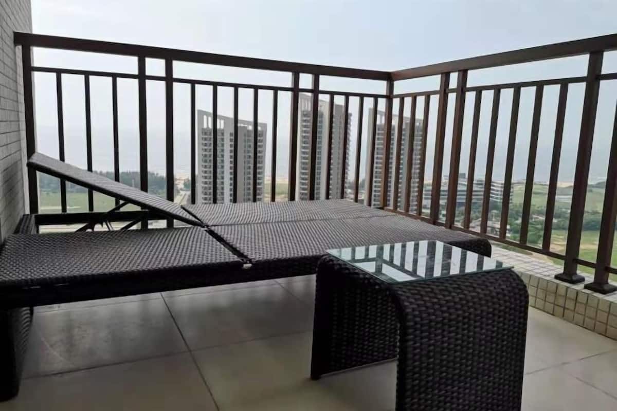Ein Balkon mit Glastisch und Korbmöbeln, mit Blick auf eine Skyline mit Hochhäusern.