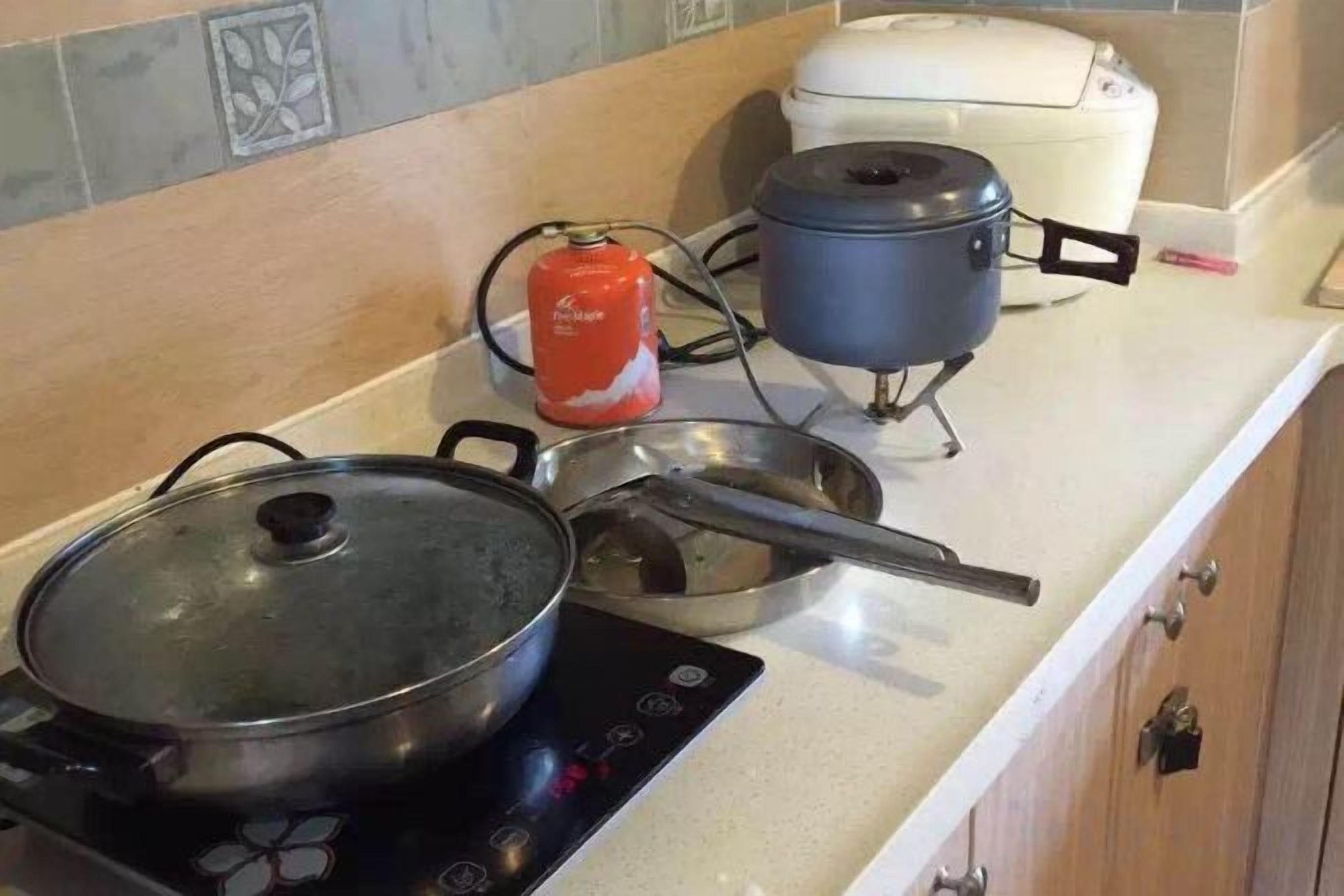 A kitchen with a stove, pots, and a rice cooker on the countertop.