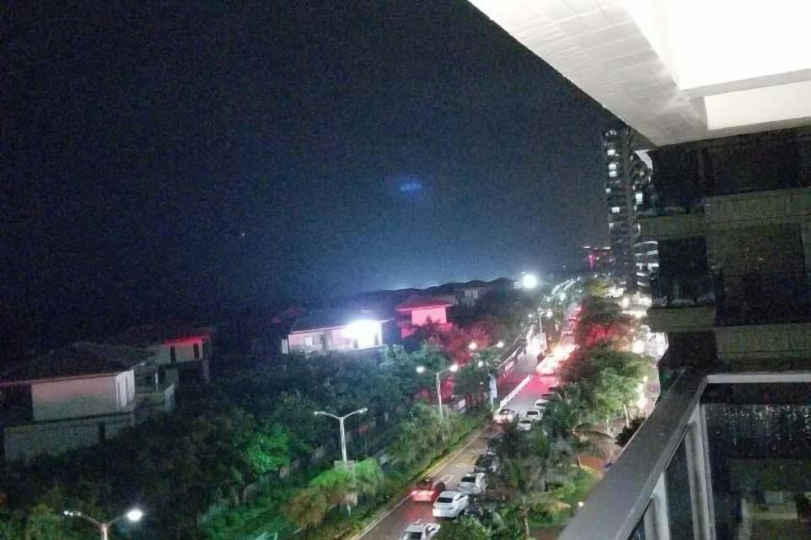 A nighttime view of a street with buildings and parked cars.