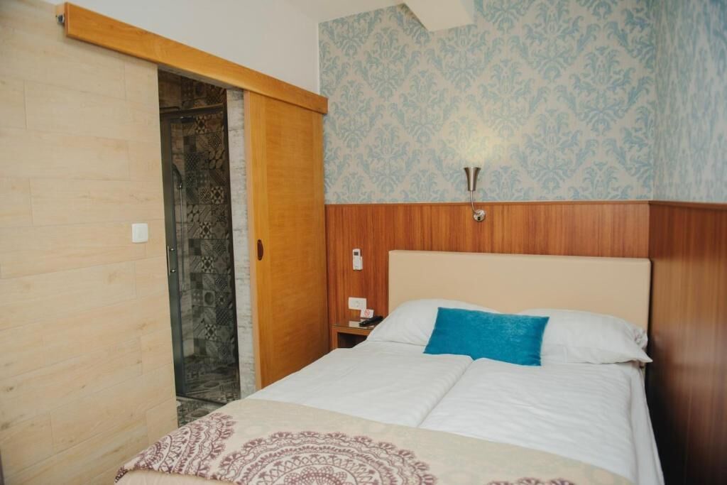 Un dormitorio con cabecera de madera, pared con diseño, cama con ropa de cama blanca y azul, y mesita de noche con teléfono y lámpara.