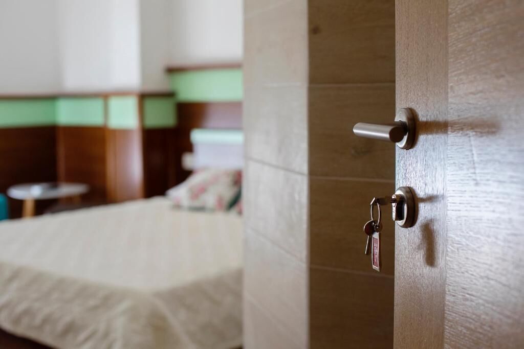 Une chambre d’hôtel avec un lit, une porte en bois dotée d’un trou de serrure et une petite table ronde à l’arrière-plan.