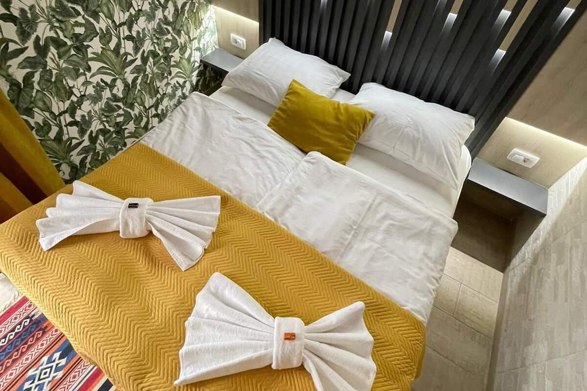 A hotel room with a bed, a yellow bedspread, and a decorative pillow.