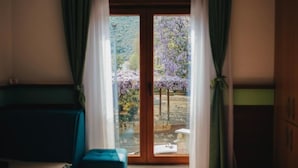 A room with a large sliding glass door leading to a garden with purple flowering trees. - Hotel Villa Lejla (Mostar)