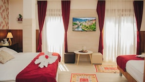 A hotel room with two beds, a small table with a vase, a wall-mounted TV, and a window with curtains. - Hotel Villa Lejla (Mostar)