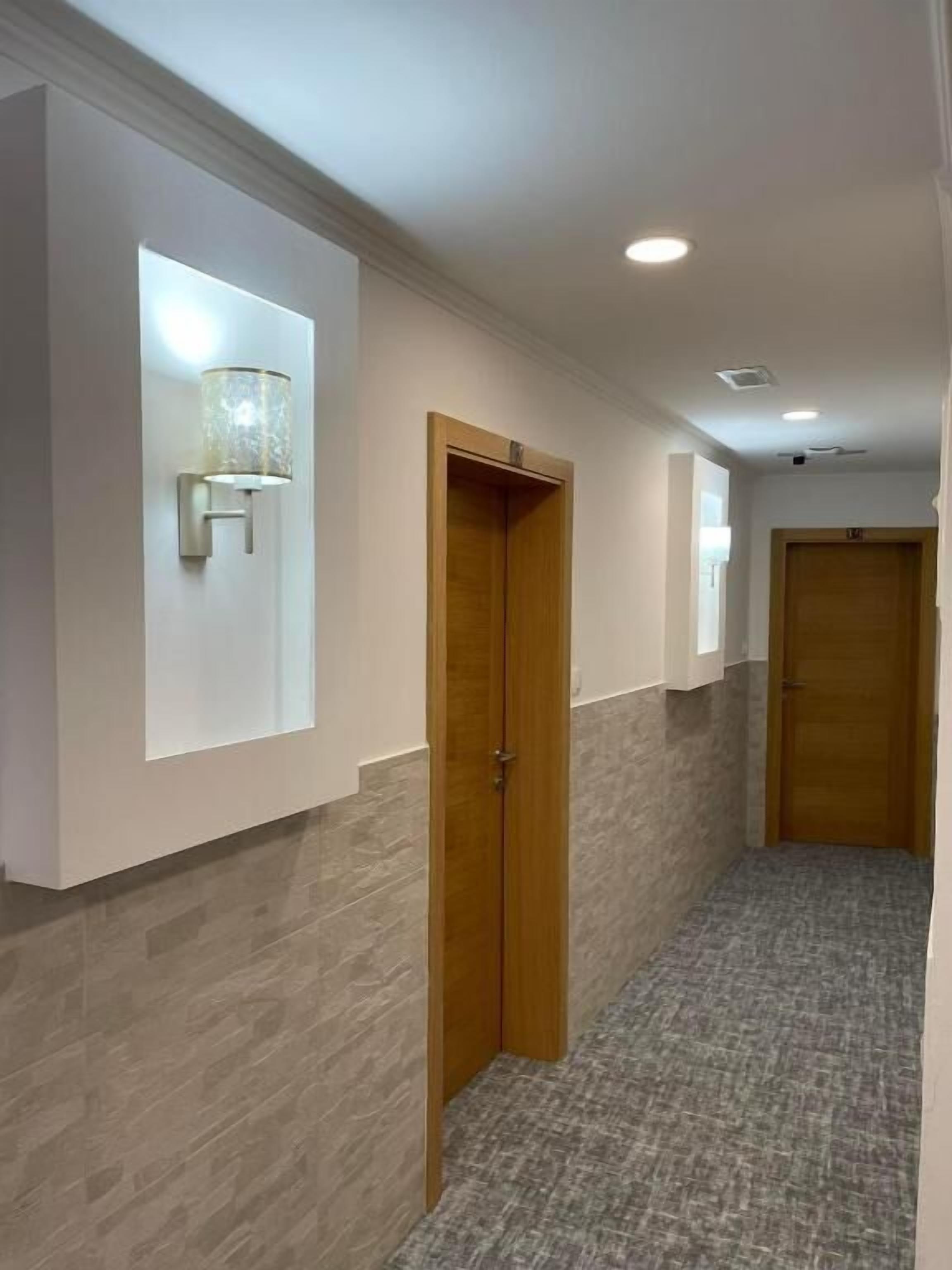 A hallway with a wooden door, a wall-mounted light fixture, and a textured floor.