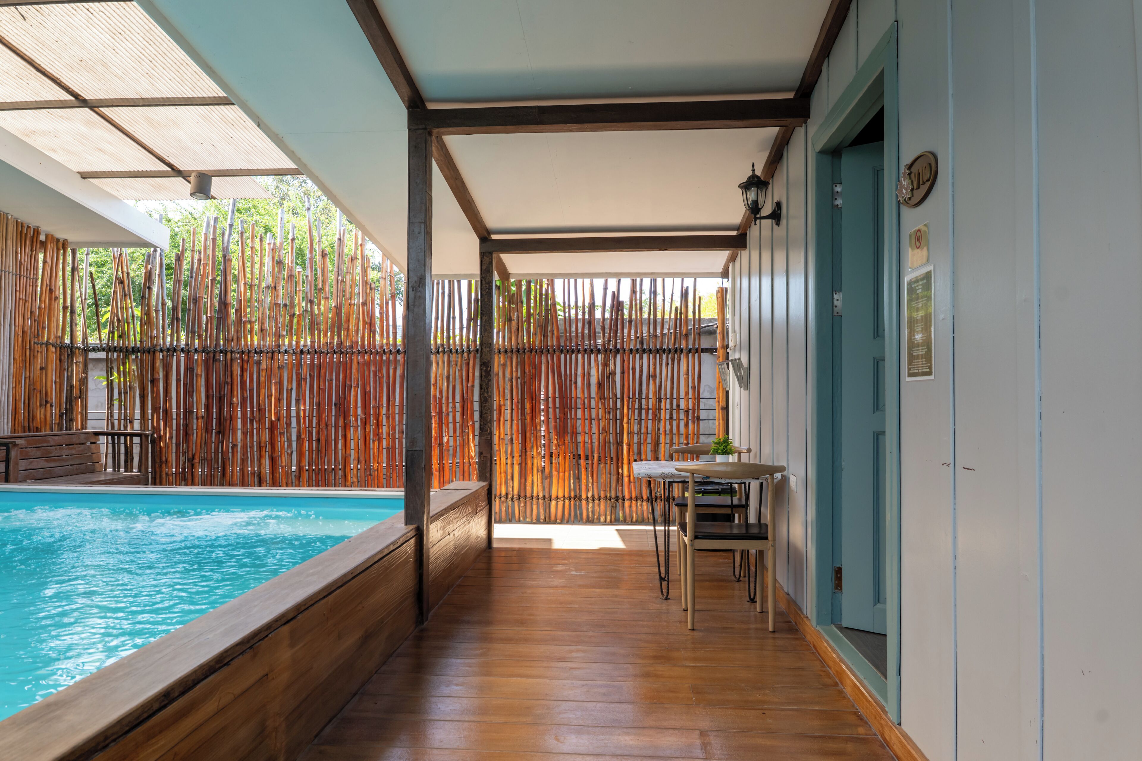 A wooden deck with a pool, bamboo fence, and a table with chairs.