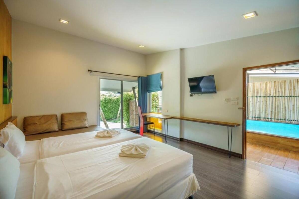 Une chambre d’hôtel avec deux lits, une télévision, un balcon donnant sur la piscine et une porte coulissante donnant sur l’extérieur.