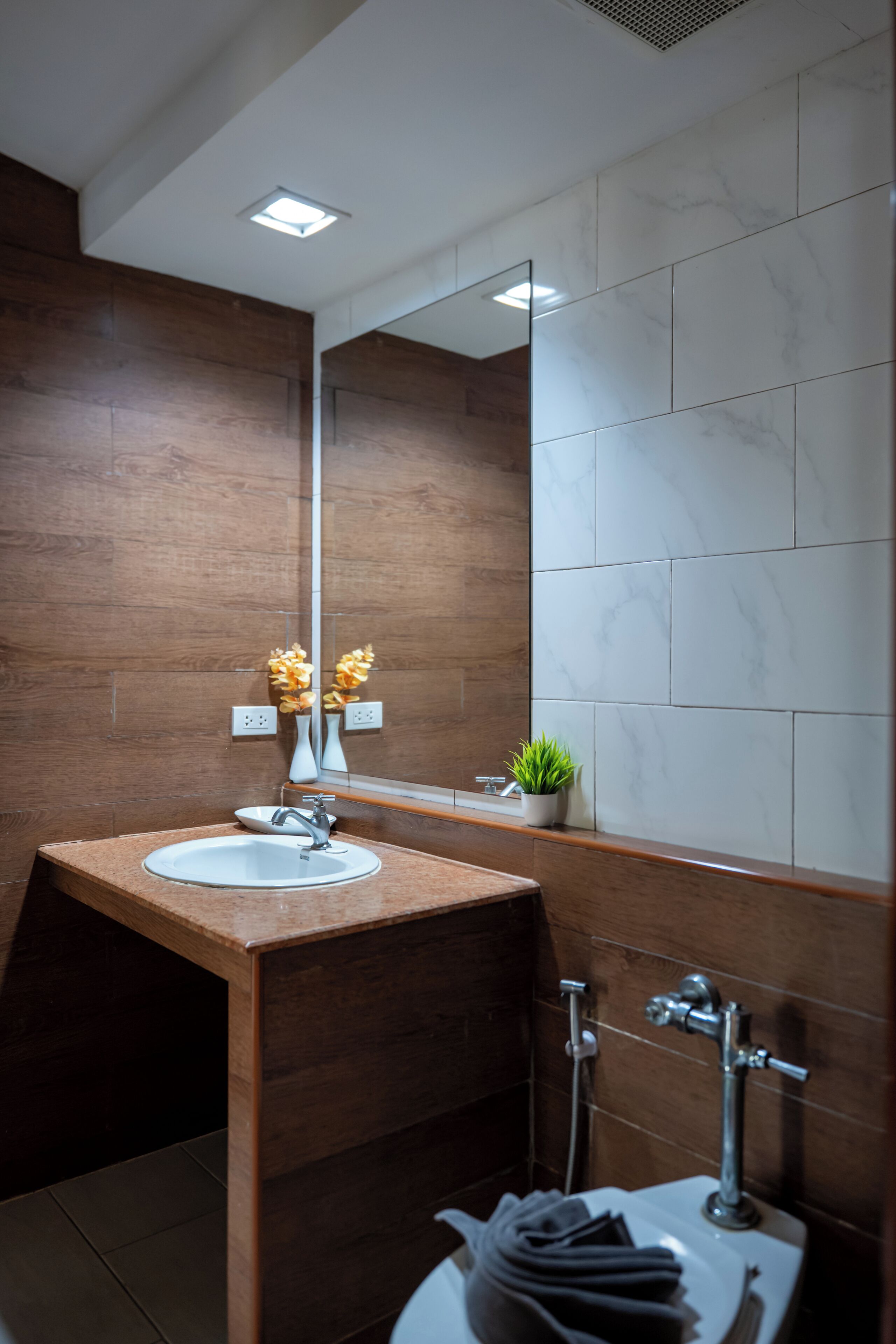 A modern bathroom with a wooden vanity, a white sink, a mirror, and a shower area.