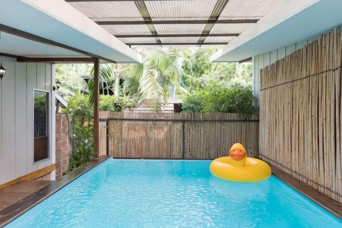 Piscina interna com cerca de bambu, um flutuador amarelo e vista para o verde lá fora.
