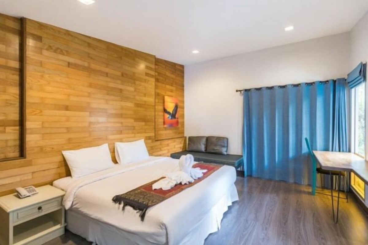 Quarto de hotel com parede de madeira, cama com roupa de cama branca, mesa de cabeceira com telefone e janela com cortinas azuis.