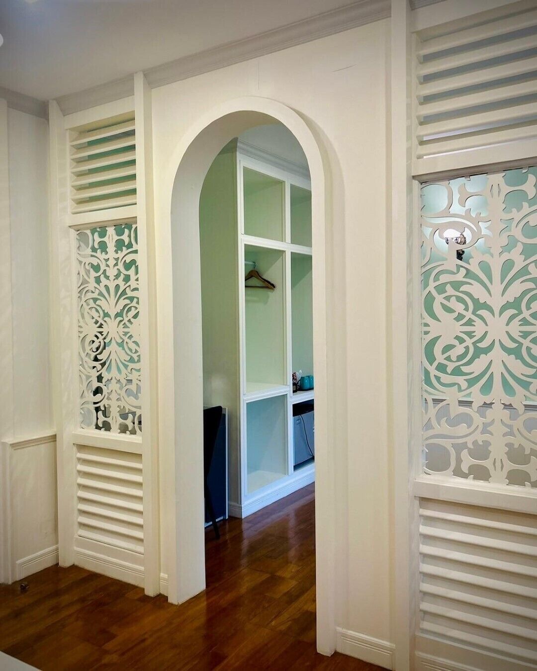 A hallway with white walls, wooden flooring, and decorative white panels on the walls.