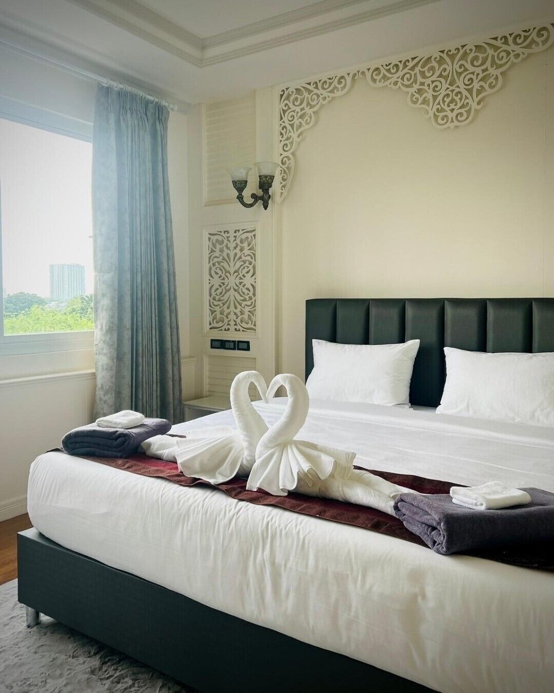 A hotel room with a large bed, a view of the city, and a decorative wall panel.