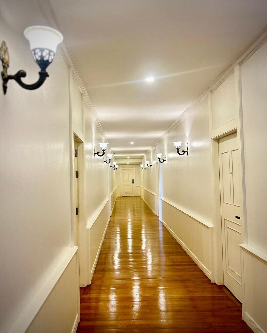 A long, narrow hallway with wooden flooring and white walls.