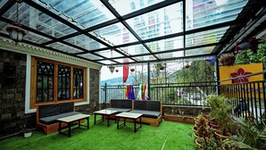 Ein Wintergarten mit Glasveranda, eine Sitzecke mit einer Bank und Tischen sowie Kübelpflanzen.